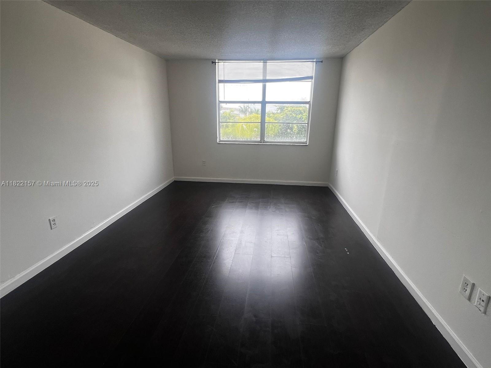 An empty room features dark wood flooring, white walls, and a single window — 498 NW 165th St Rd # D303, Miami FL 33169, MIAMI, FL