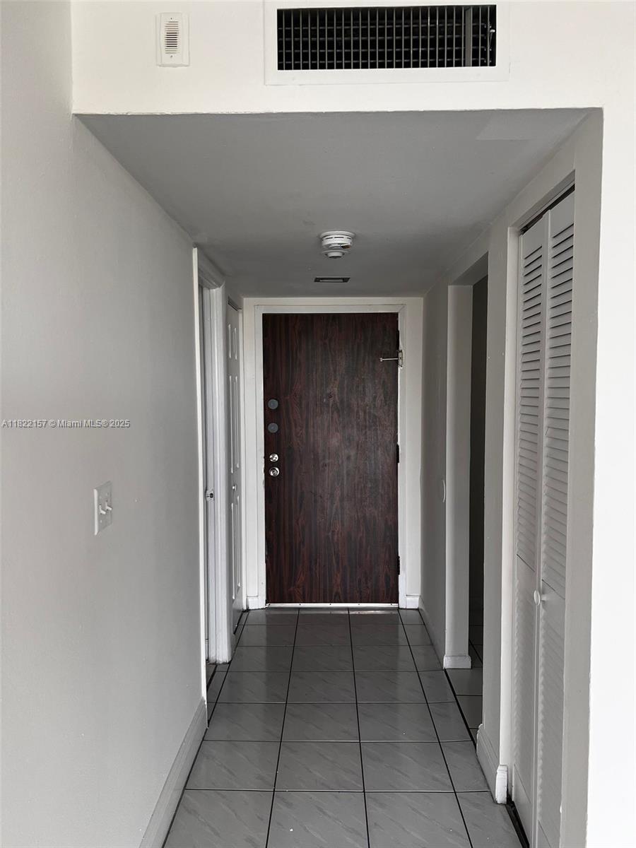 A hallway with gray tile flooring leads to a dark wood front door — 498 NW 165th St Rd # D303, Miami FL 33169, MIAMI, FL