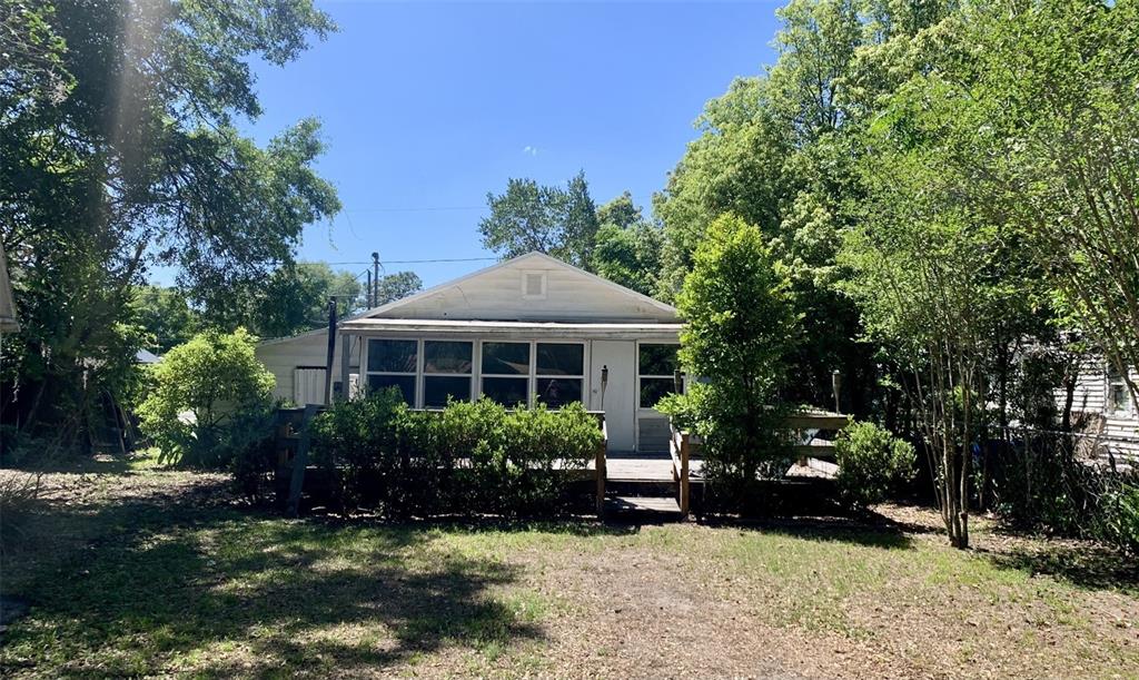 A white house with a wooden deck and surrounding trees sits in a grassy yard — 4836 19TH STREET, ZEPHYRHILLS, FL