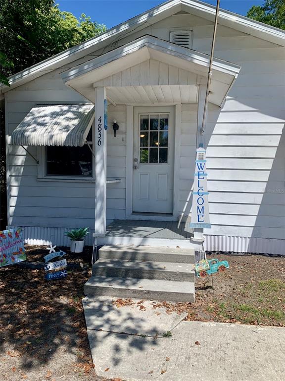 The exterior of a white house features a covered front porch with concrete steps — 4836 19TH STREET, ZEPHYRHILLS, FL