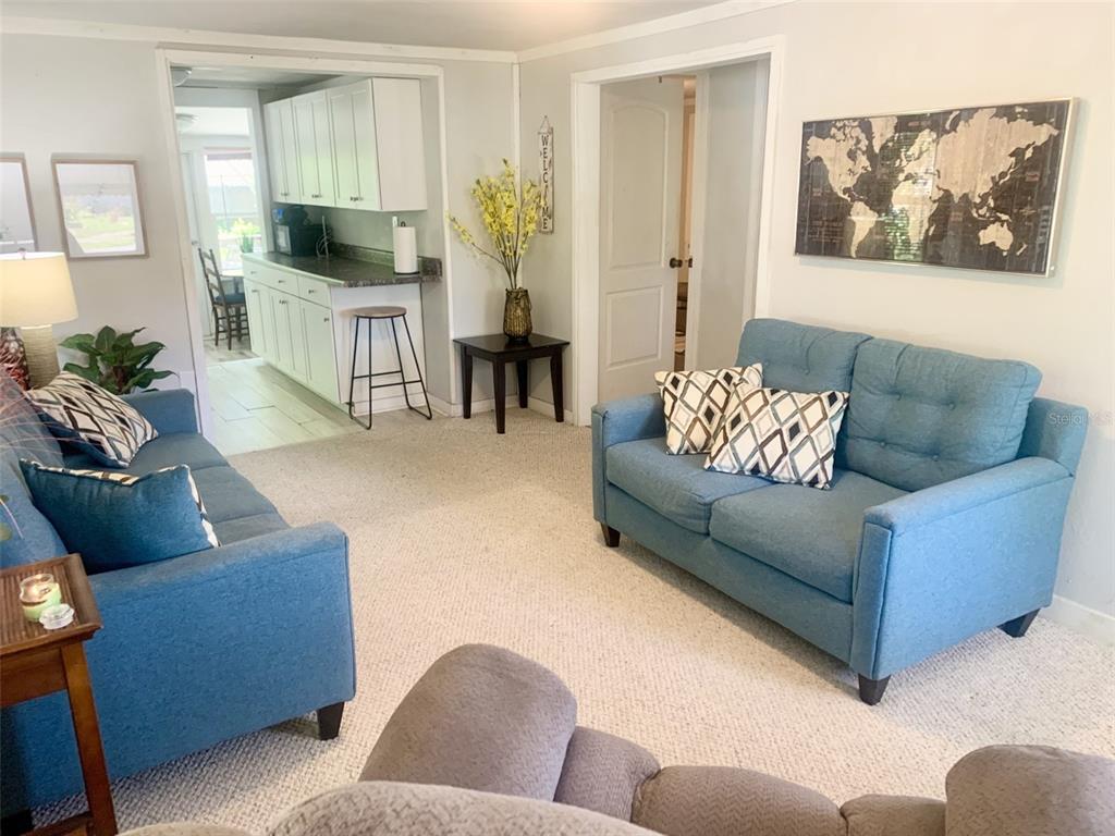 A living room features two blue sofas, a world map wall art, and an adjacent kitchen — 4836 19TH STREET, ZEPHYRHILLS, FL