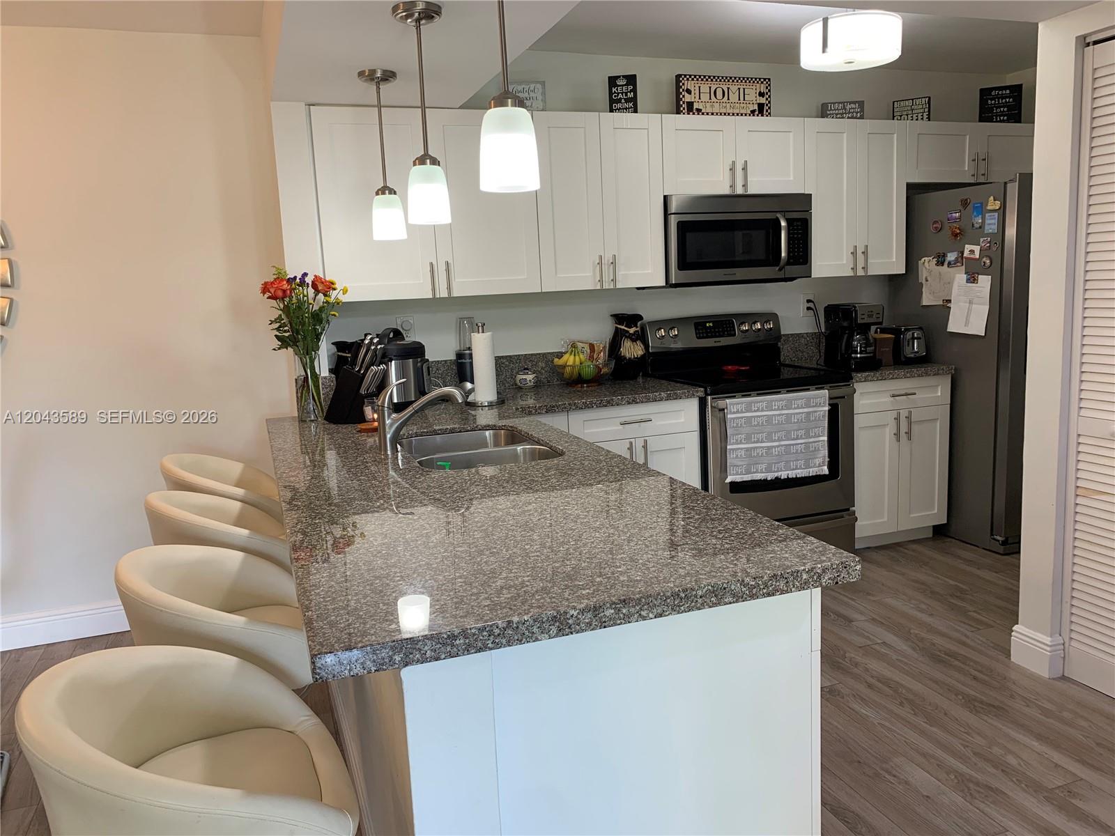 A kitchen features white cabinets, granite countertops, a breakfast bar with four chairs, and stainless appliances — 8660 SW 212th St # 305, Cutler Bay FL 33189, CUTLER BAY, FL
