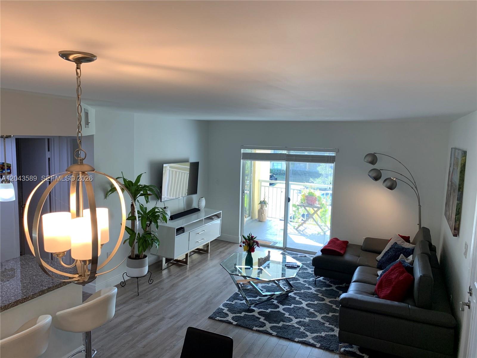 A living room features a sectional sofa, glass coffee table, media console, and balcony access — 8660 SW 212th St # 305, Cutler Bay FL 33189, CUTLER BAY, FL