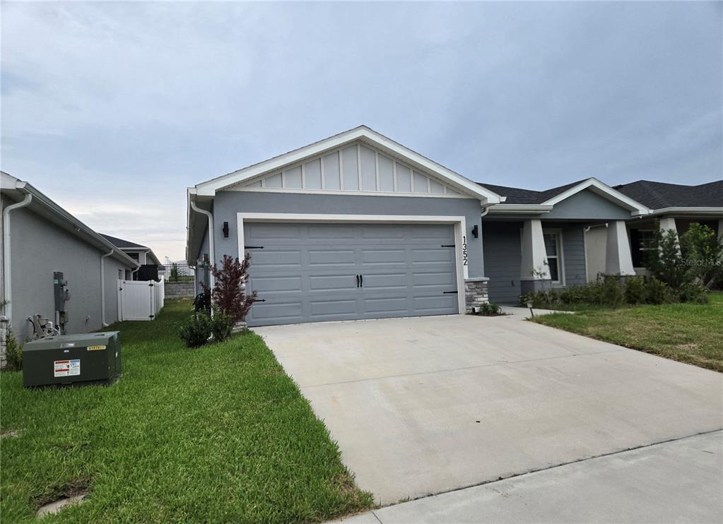 A gray single-story house features a two-car garage, a concrete driveway, and a grassy lawn — 1352 MOUNTAIN FLOWER LANE, DAVENPORT, FL