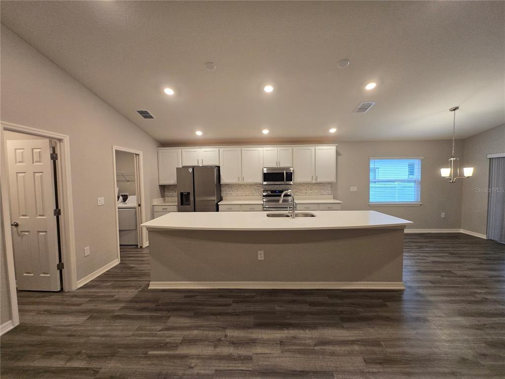 A kitchen features white cabinetry, stainless steel appliances, a large island, and wood-look flooring — 1352 MOUNTAIN FLOWER LANE, DAVENPORT, FL