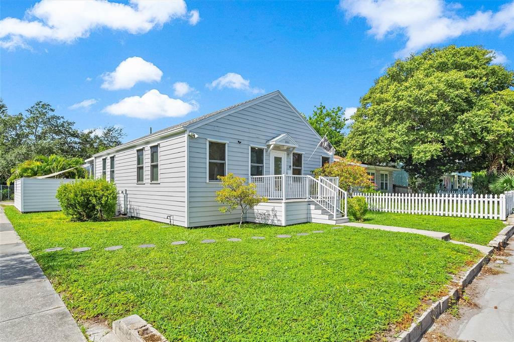 A light blue, single-story house with a white porch and picket fence sits on grass — 1500 9TH AVENUE N, ST PETERSBURG, FL