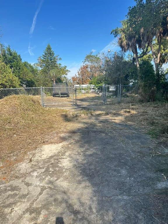 A fenced, unpaved lot with a concrete driveway and scattered vegetation under a blue sky — 4637 COTTONWOOD DRIVE, NEW PORT RICHEY, FL