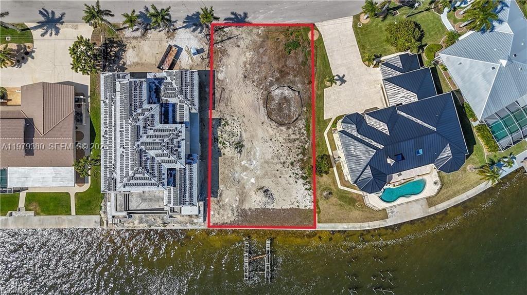 An aerial view shows a vacant waterfront lot outlined in red between two residential properties — CAPE CORAL, FL