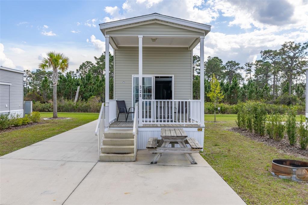 A small, light-green mobile home features a covered front porch, stairs, and a wooden picnic table — 325 TIKI TURN (HWY 630) E, LAKE WALES, FL