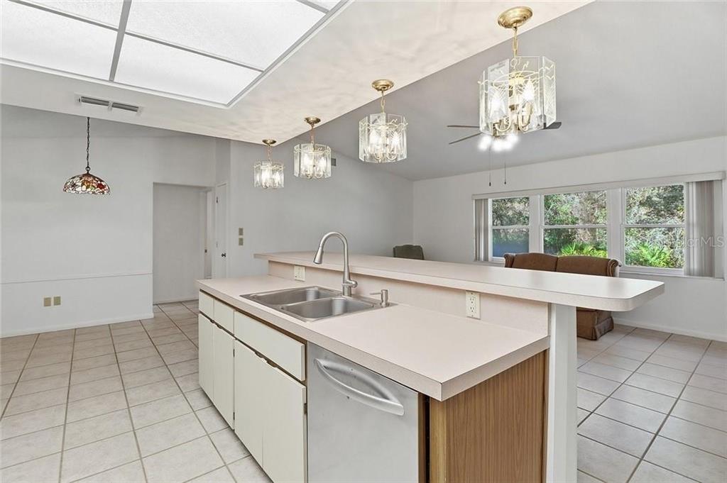 A kitchen features a breakfast bar, light-colored cabinets, tile flooring, and multiple hanging light fixtures — 36 PINE DRIVE, HOMOSASSA, FL