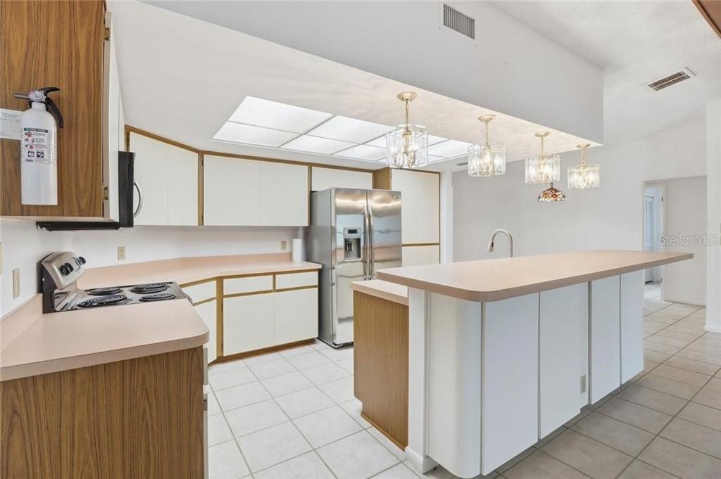 A kitchen features white cabinets, laminate countertops, stainless steel appliances, and a breakfast bar — 36 PINE DRIVE, HOMOSASSA, FL