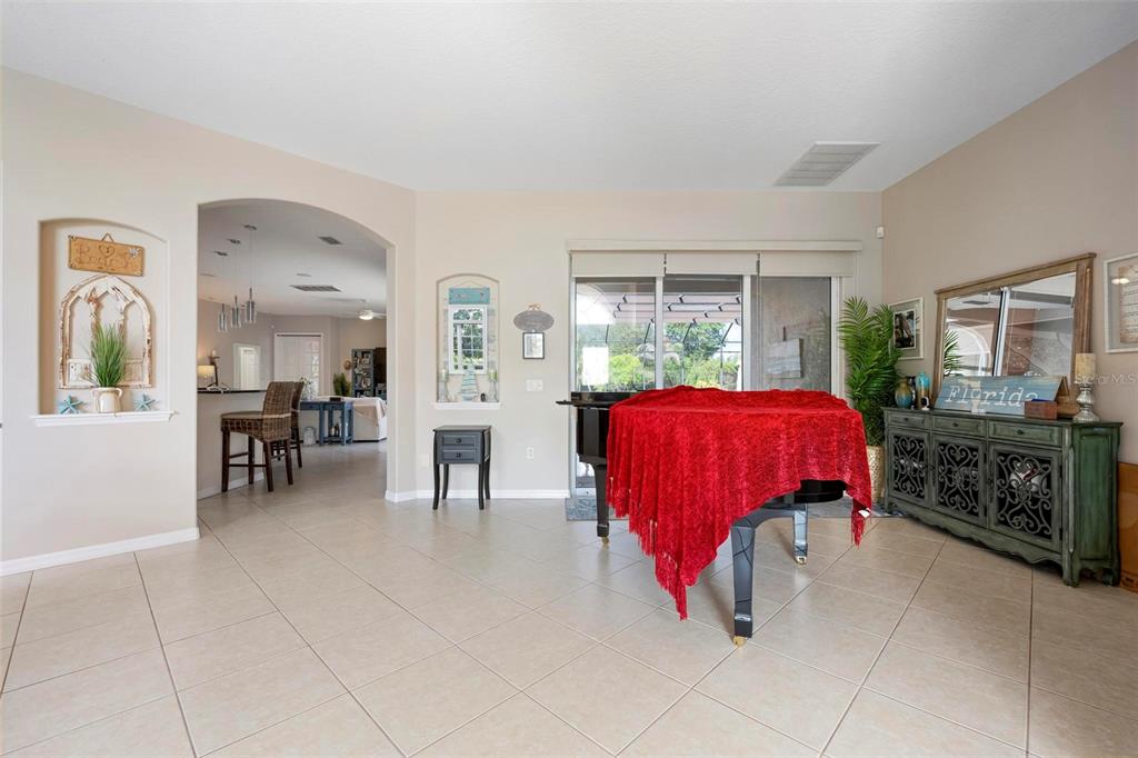 A living room features a grand piano covered by a red cloth and tile flooring — 22610 NIGHT HERON WAY, BRADENTON, FL