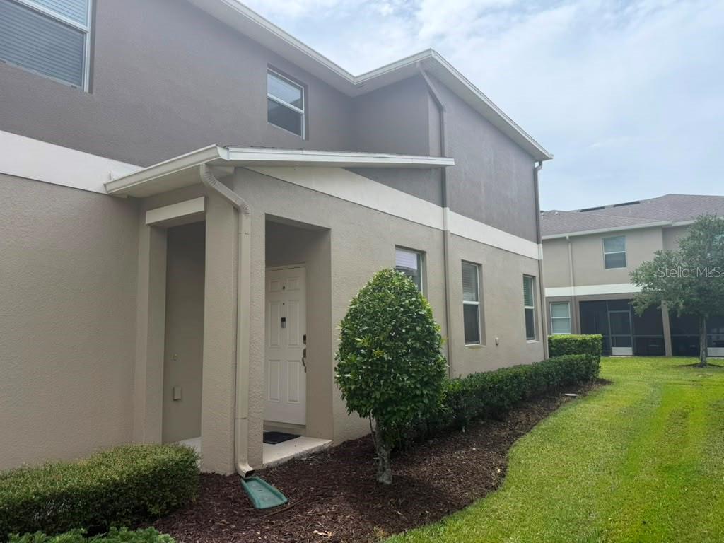 A two-story townhouse exterior features a covered entryway, tan stucco walls, and a small lawn — 15222 HARRINGTON COVE DRIVE, ORLANDO, FL