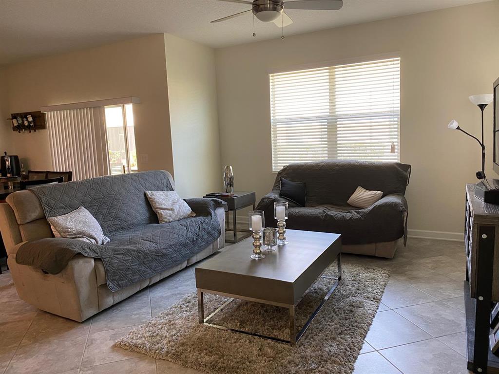 A living room features two sofas with gray covers, a coffee table, and tile flooring — 15222 HARRINGTON COVE DRIVE, ORLANDO, FL