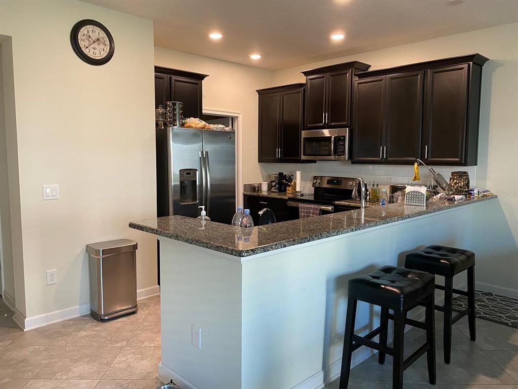 A kitchen features dark wood cabinets, granite countertops, stainless steel appliances, and a breakfast bar — 15222 HARRINGTON COVE DRIVE, ORLANDO, FL