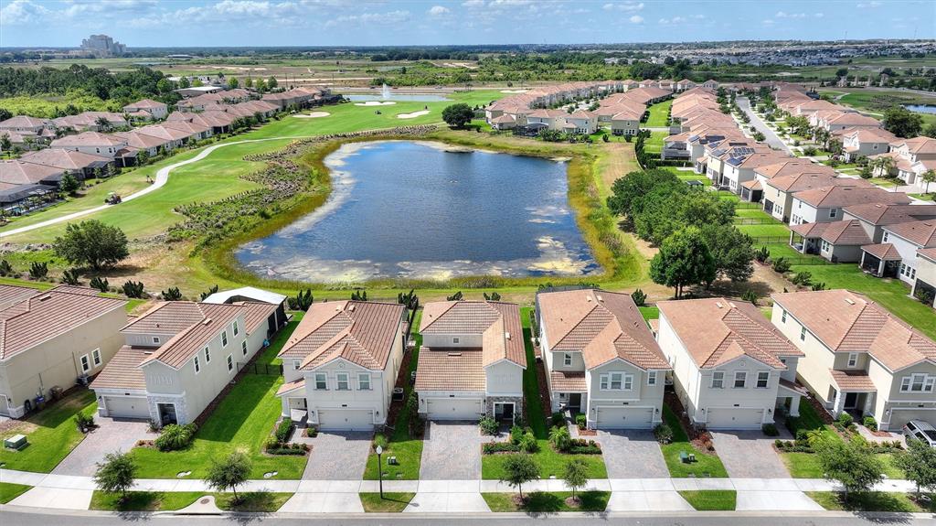 An aerial view shows a suburban neighborhood with houses bordering a central pond and golf course — 8736 PACIFIC DUNES DR, DAVENPORT, FL
