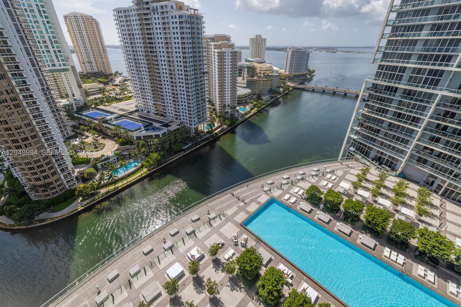 High-angle view of a luxury apartment building pool deck overlooking a canal and city skyline — 465 Brickell Ave # 3506, Miami FL 33131, MIAMI, FL