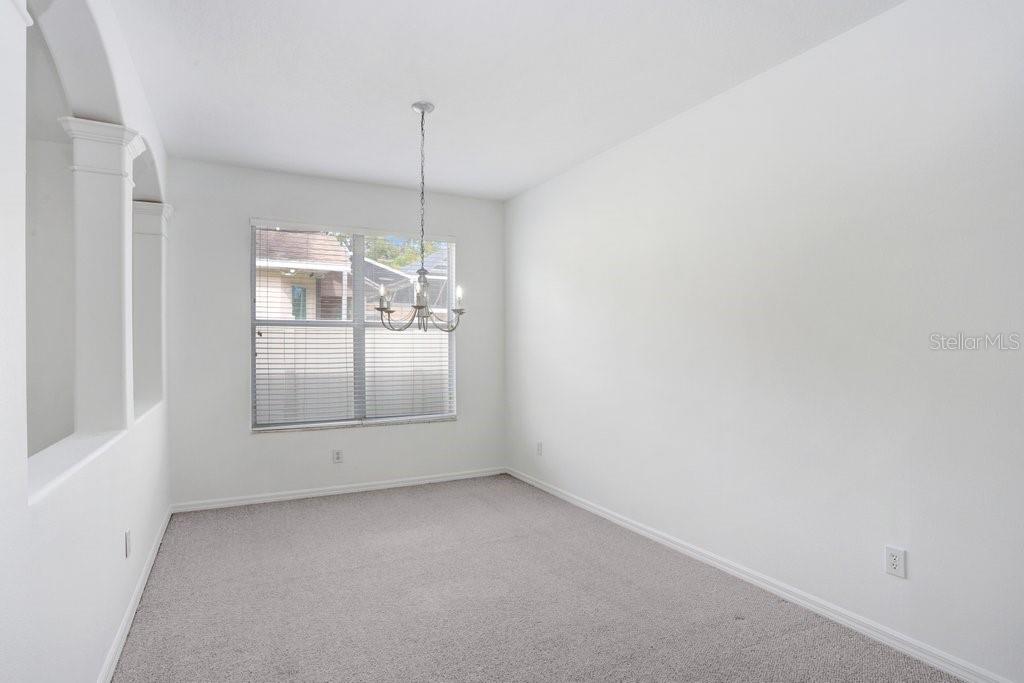 A dining room with white walls, gray carpet, a chandelier, and a window with blinds — 2927 MINUTEMAN LANE, BRANDON, FL