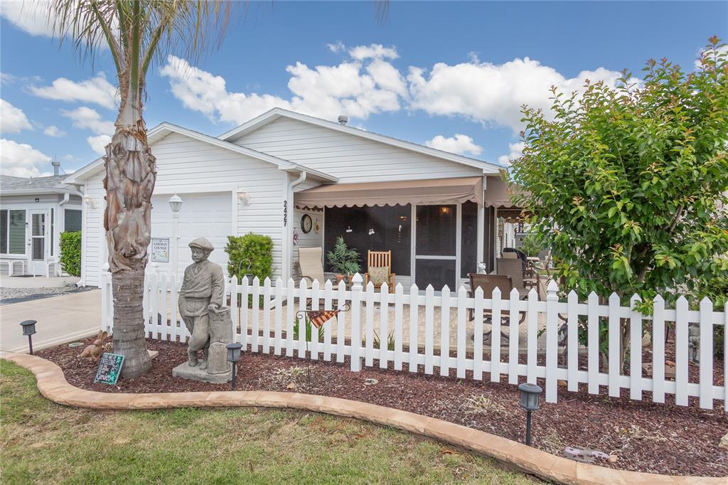A white house with a picket fence, a palm tree, and a statue in front — 2427 SOUTHERN OAK STREET, THE VILLAGES, FL