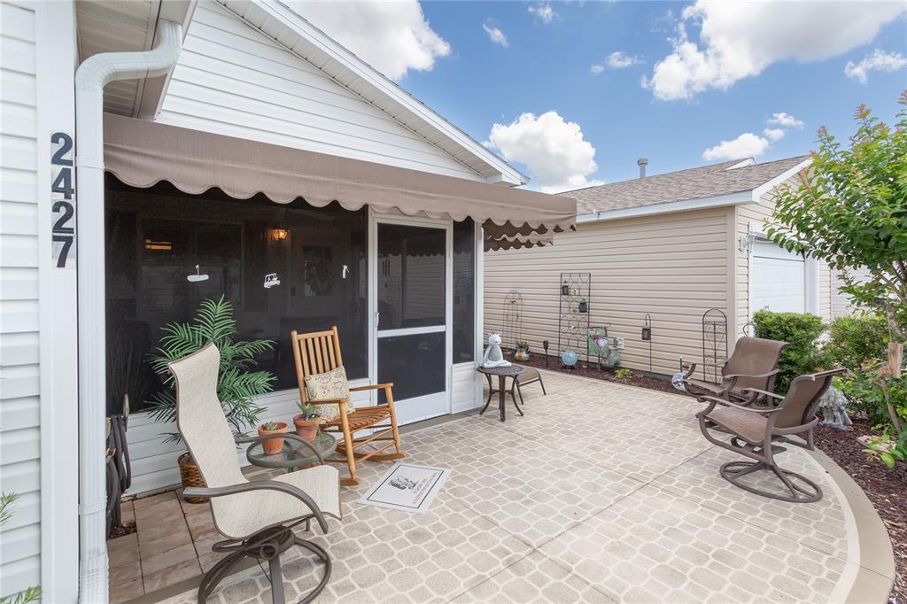 A patio with outdoor furniture sits in front of a house with a screened porch — 2427 SOUTHERN OAK STREET, THE VILLAGES, FL
