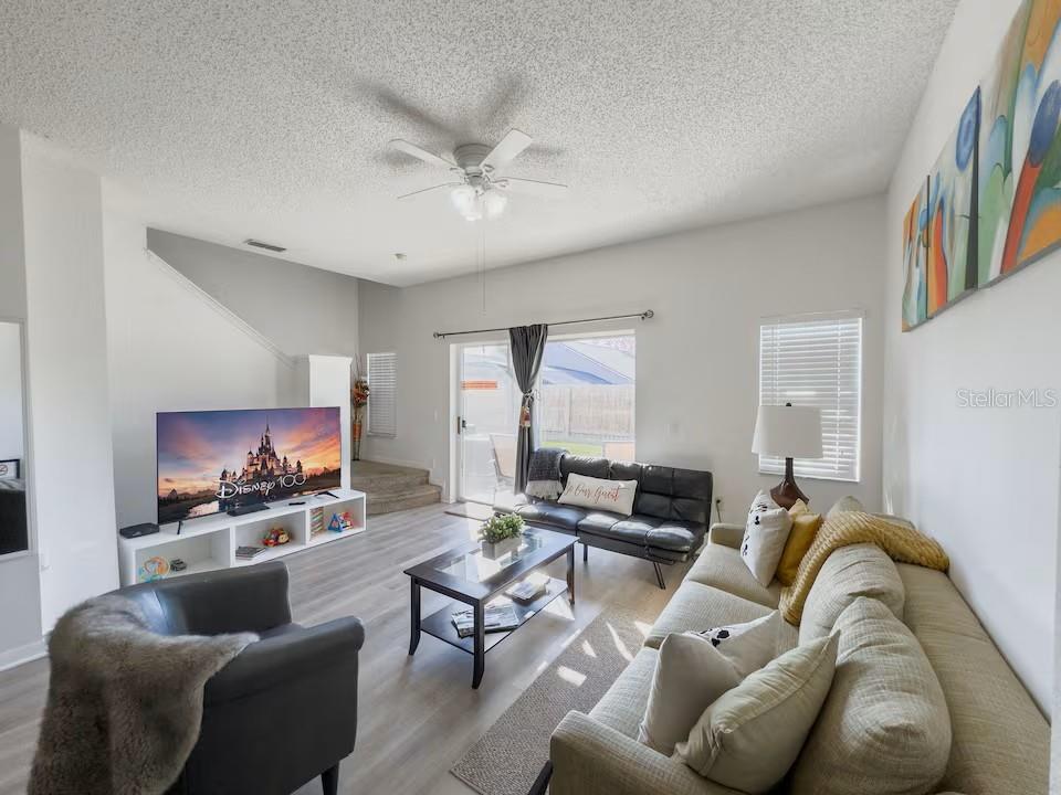 A living room features light wood-look flooring, a ceiling fan, a television, and neutral furniture — 910 PARK TERRACE CIRCLE, KISSIMMEE, FL