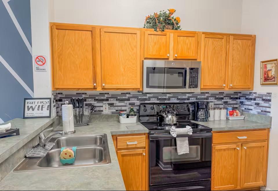 A kitchen features oak cabinets, a stainless steel microwave, a black stove, and gray countertops — 910 PARK TERRACE CIRCLE, KISSIMMEE, FL