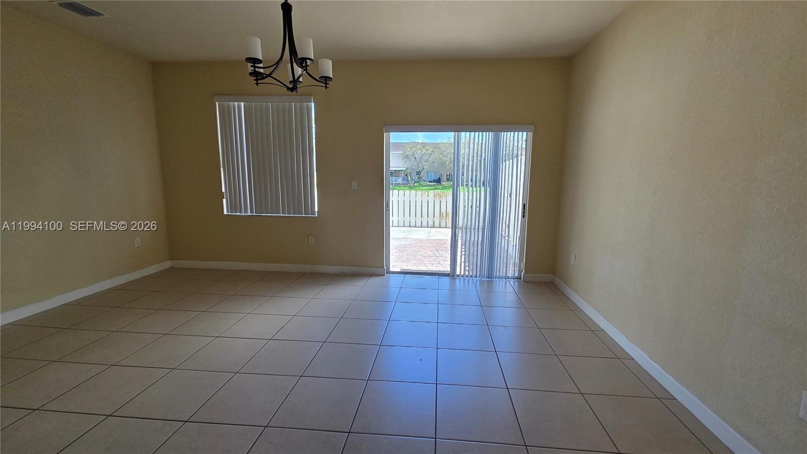 An empty dining room features beige tile flooring, a chandelier, and sliding glass patio doors — 9001 SW 227th St # 7, Cutler Bay FL 33190, CUTLER BAY, FL