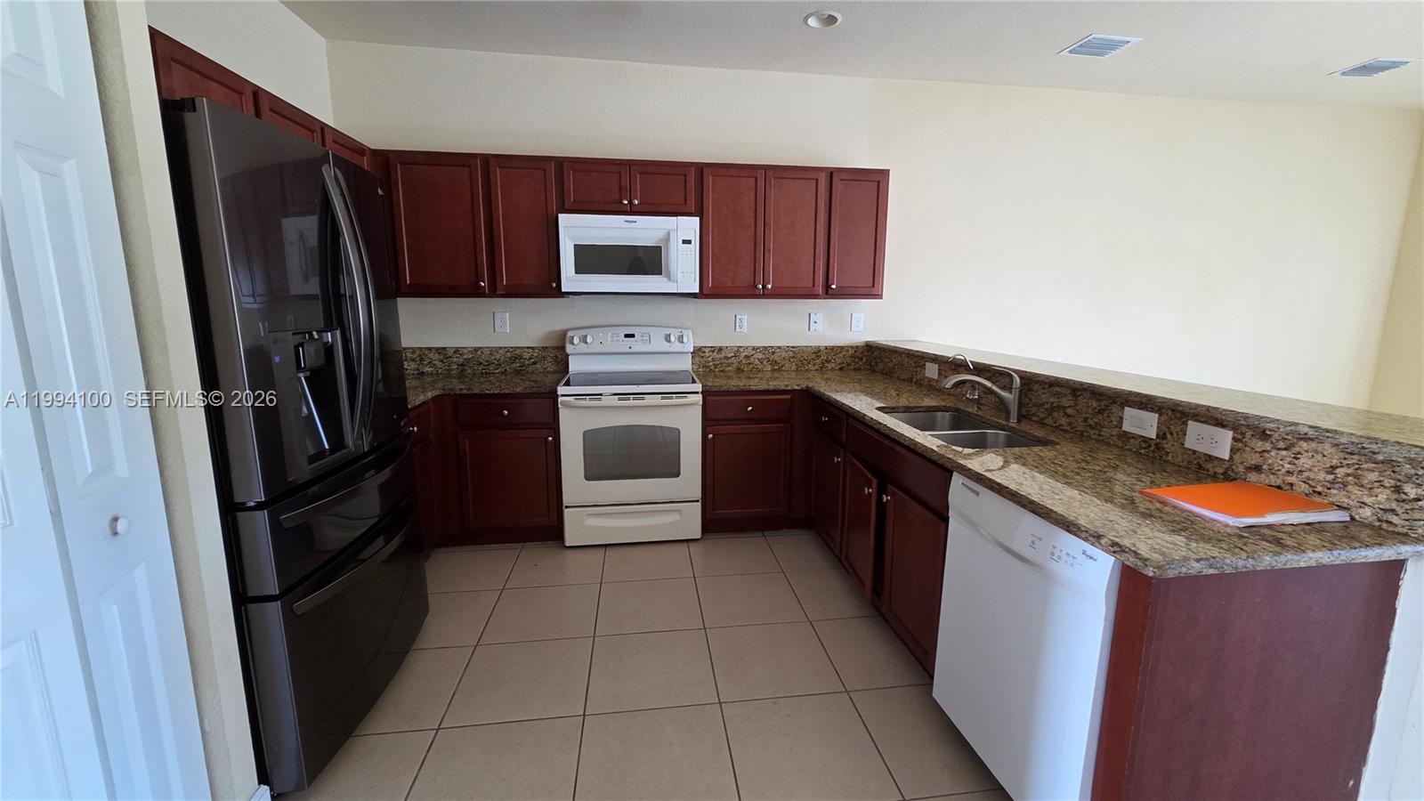 A kitchen features dark wood cabinets, granite countertops, tile flooring, and white appliances — 9001 SW 227th St # 7, Cutler Bay FL 33190, CUTLER BAY, FL