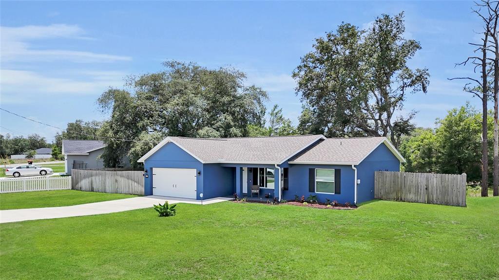 A blue single-story house with a white garage door, gray roof, and a wooden fence — 20 MALAUKA CIRCLE, OCKLAWAHA, FL