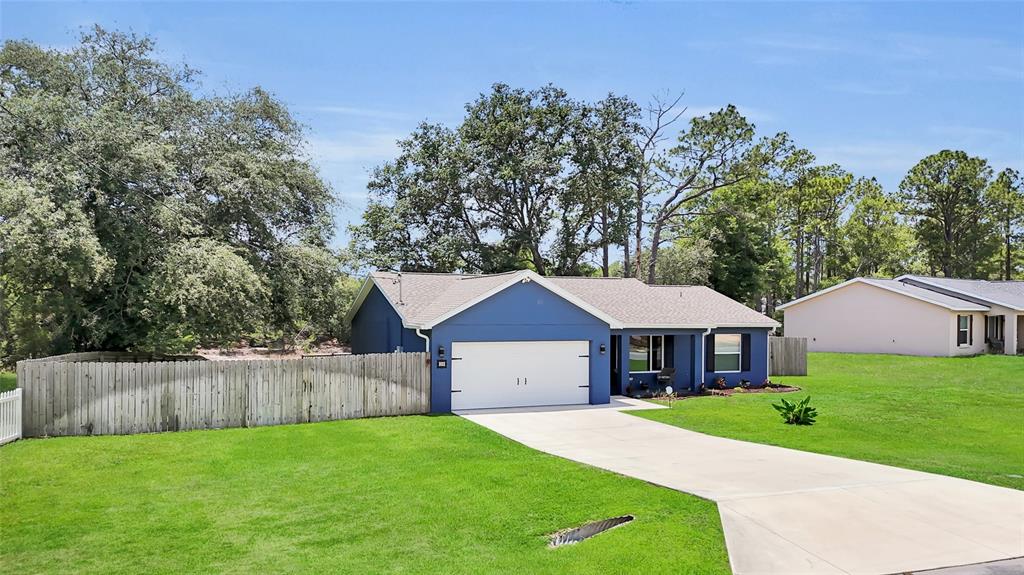 A blue single-story house with a white garage door and a wooden fence — 20 MALAUKA CIRCLE, OCKLAWAHA, FL
