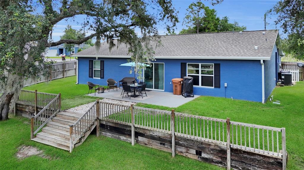 The exterior of a blue house features a concrete patio, wooden deck, and backyard lawn — 20 MALAUKA CIRCLE, OCKLAWAHA, FL