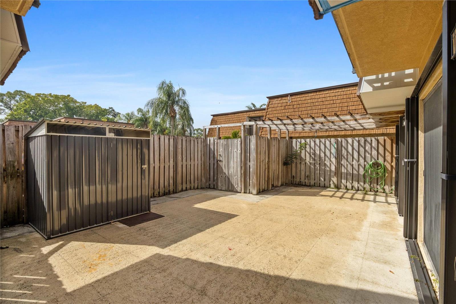 A concrete patio features a metal storage shed, a wooden fence, and a pergola — 1821 18th Lane, FL 33463, FL