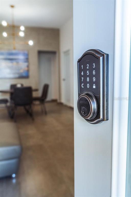 A close-up of a digital keypad deadbolt on a door frame, with a dining area blurred in the background — 117 CALLE POMARROSA UNIT 3D, SAN JUAN, PR