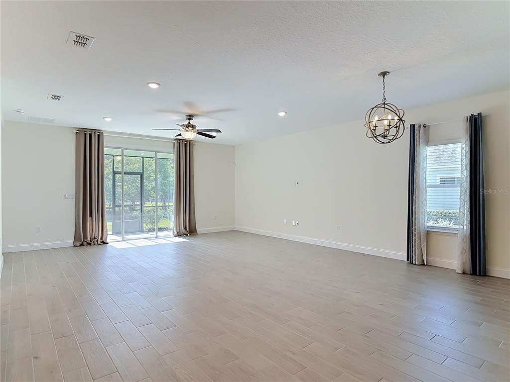 A spacious living room features light wood-look tile flooring, a ceiling fan, and sliding glass doors — 2183 RAGLAN CIRCLE, ORMOND BEACH, FL