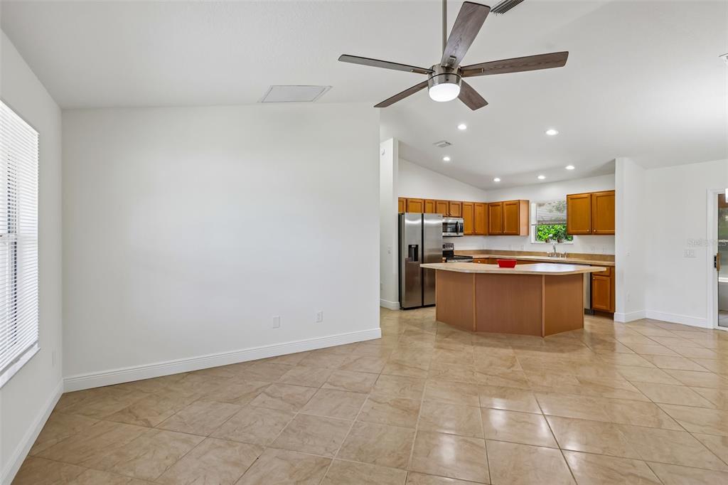 An open-concept kitchen with wood cabinets and a central island overlooks a tiled living area — 1000 KENOVA AVENUE, THE VILLAGES, FL