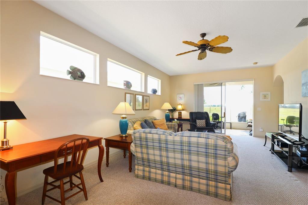 A living room features a plaid sofa, a wooden desk, and large sliding glass doors — 20846 QUEEN ALEXANDRA DRIVE, LEESBURG, FL