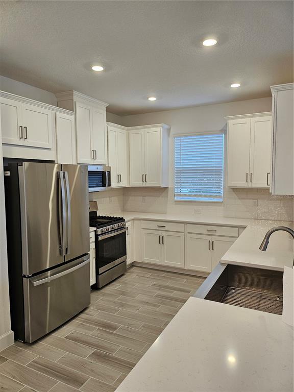 A kitchen features white cabinets, stainless steel appliances, quartz countertops, and light wood-look tile flooring — 10057 MORNING MIST LANE, SARASOTA, FL