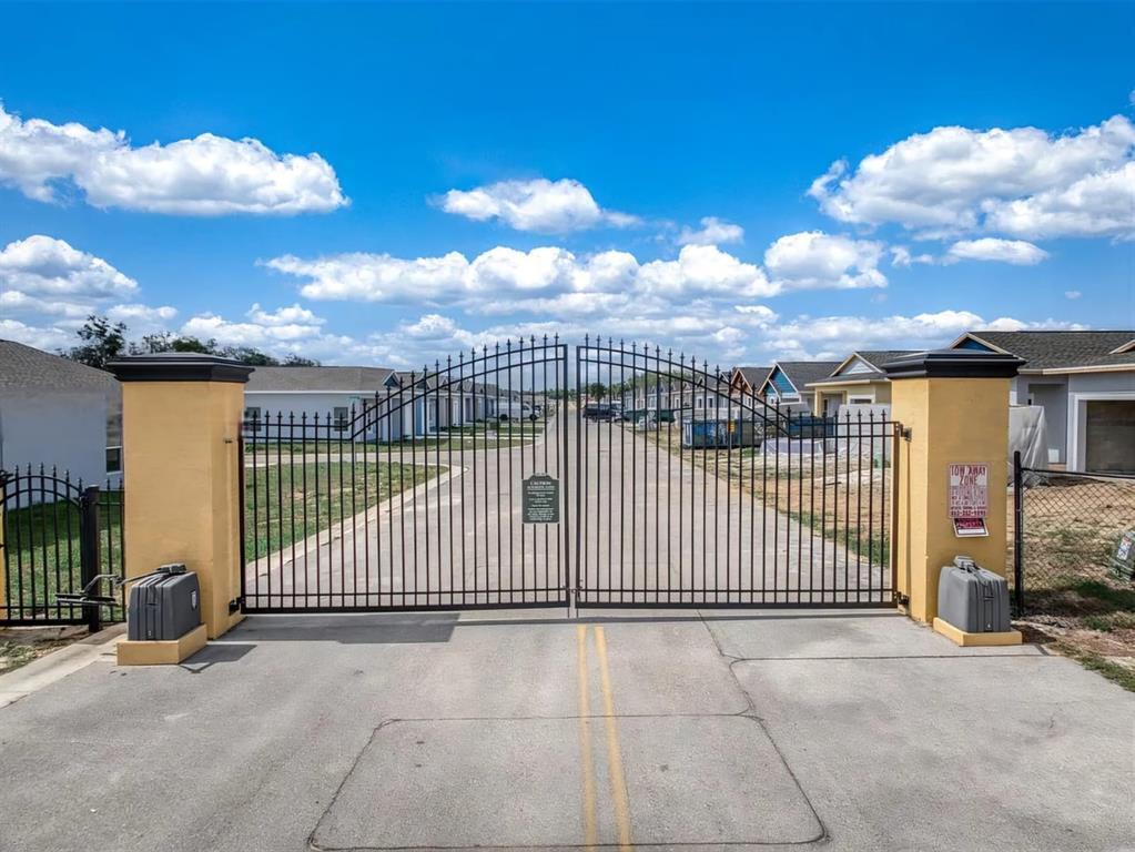 A gated entrance with two yellow pillars leads to a residential street under a blue sky — 1450 Las Villas Boulevard, Sebring FL 33870, SEBRING, FL