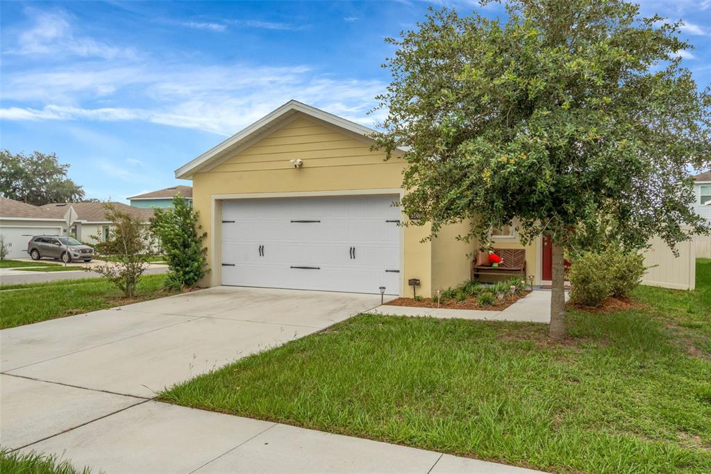 A yellow single-story house with a two-car garage and a front yard with a tree — 35088 JOMAR AVENUE, ZEPHYRHILLS, FL