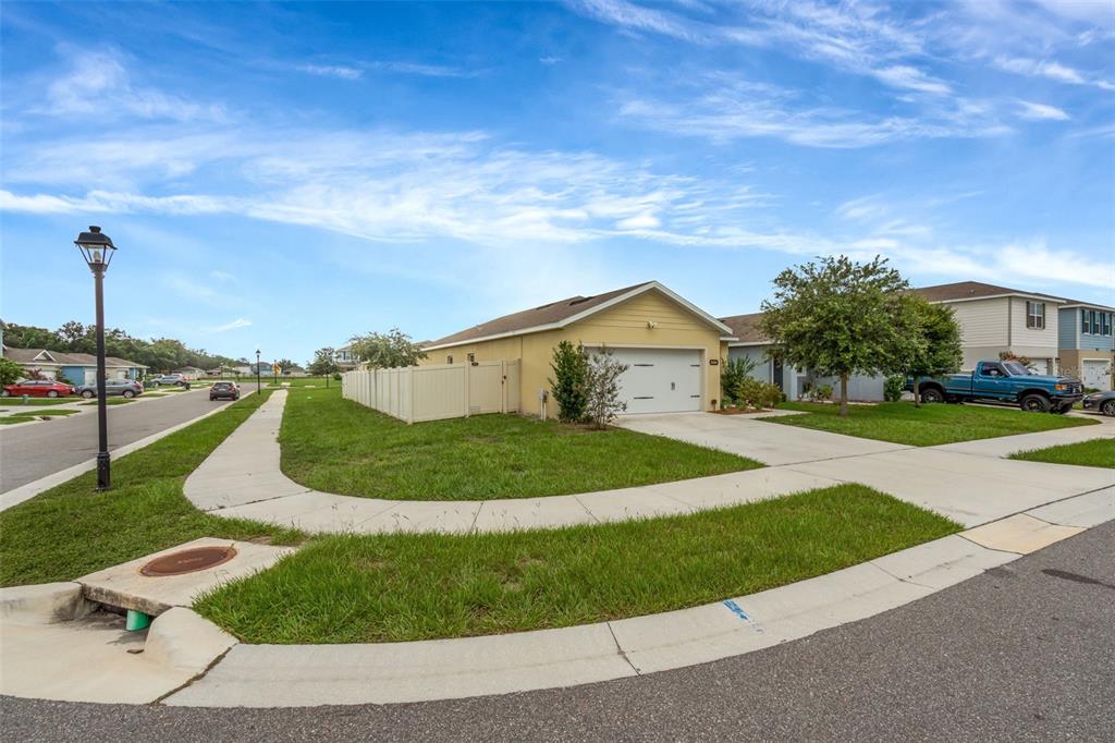 A yellow single-story house with a white garage and fence sits on a corner lot — 35088 JOMAR AVENUE, ZEPHYRHILLS, FL