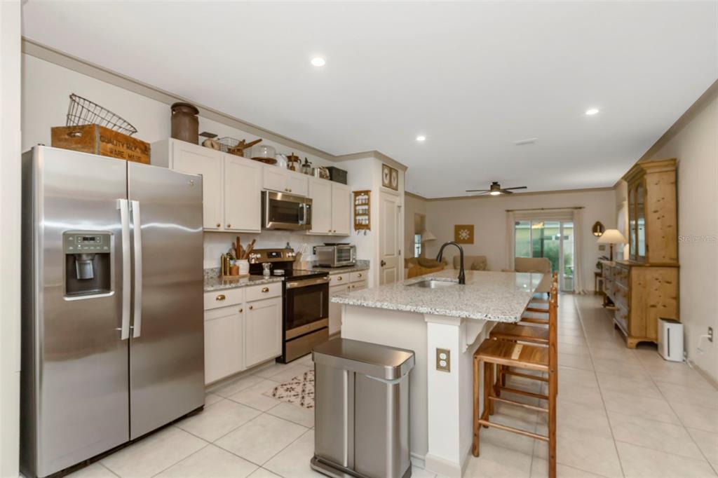 A kitchen with stainless steel appliances, granite countertops, an island with seating, and tile flooring — 35088 JOMAR AVENUE, ZEPHYRHILLS, FL