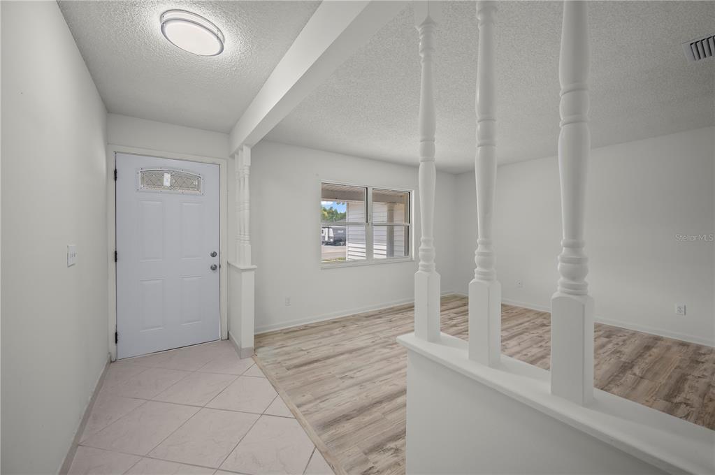 An entryway with tile flooring leads into a living area featuring wood-look floors and railings — 405 N HAWTHORN CIRCLE, WINTER SPRINGS, FL