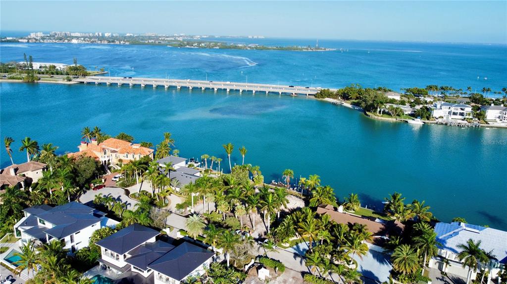 An aerial view shows luxury waterfront homes, palm trees, and a long bridge over water — 109 N WARBLER LANE, SARASOTA, FL