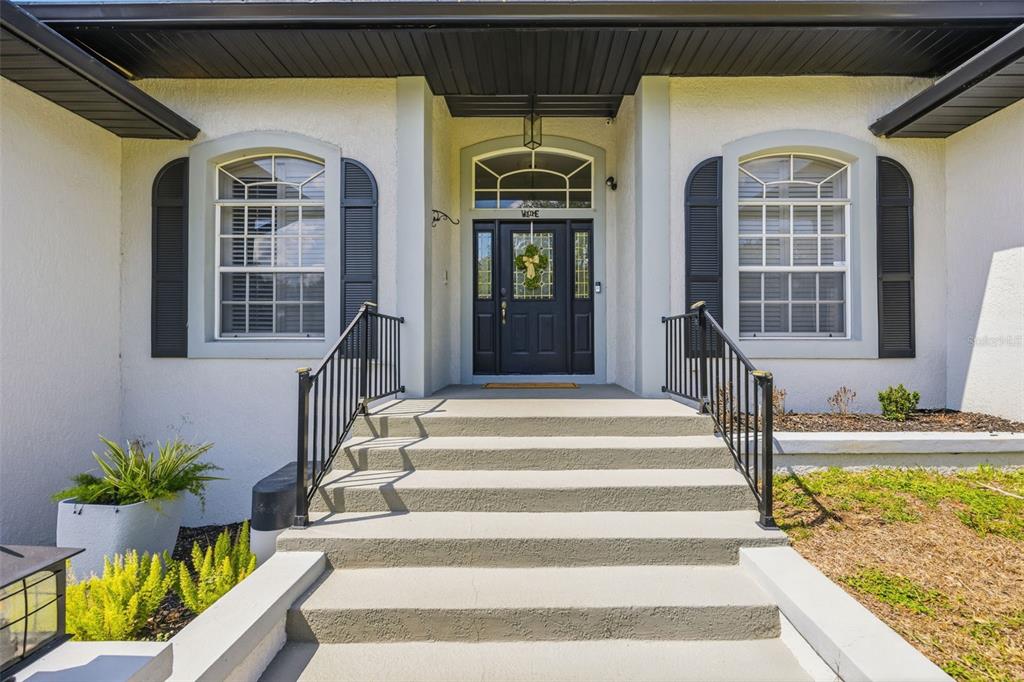 A front entrance with concrete steps, black railings, and a dark door with a transom window — 13031 SUNSHINE VIEW COURT, CLERMONT, FL