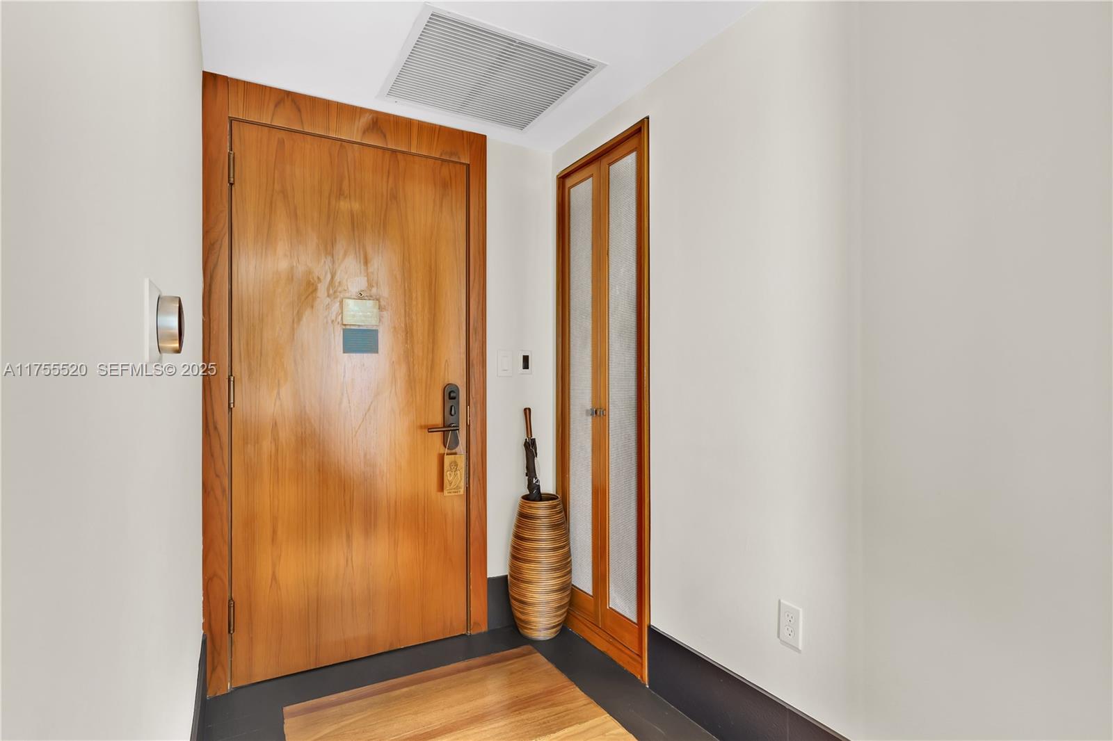 An entryway features a wooden door, a tall textured vase with an umbrella, and flooring — 101 20th St # 1803, Miami Beach FL 33139, MIAMI BEACH, FL