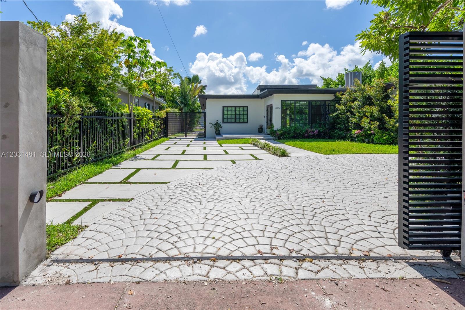 A modern house features a patterned stone driveway and a gated entrance with lush landscaping — 7850 Hawthorne Ave, Miami Beach FL 33141, MIAMI BEACH, FL