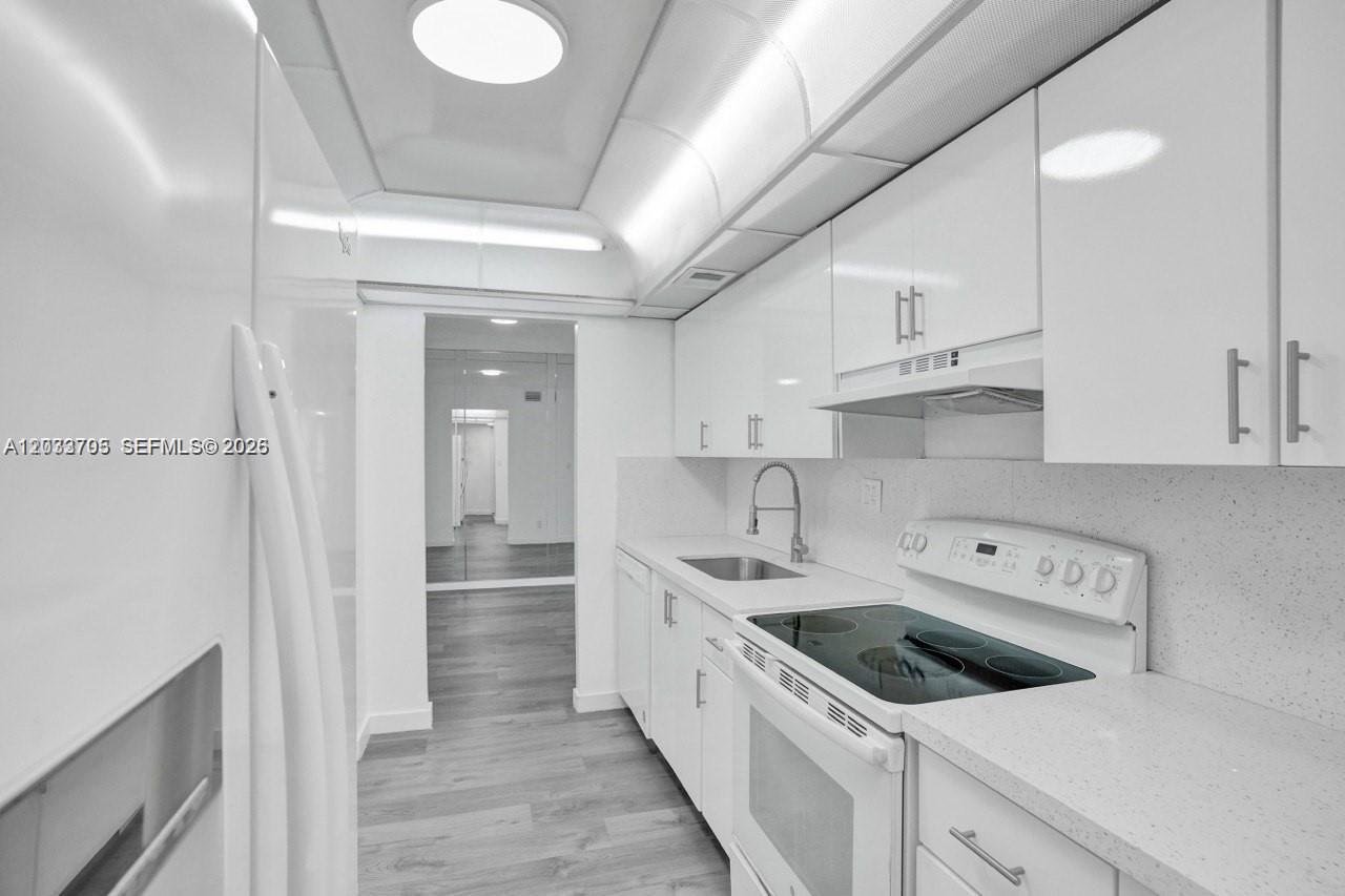 A narrow, all-white galley kitchen features glossy cabinets, a glass-top stove, and light flooring — 3821 Environ Blvd # 403, Lauderhill FL 33319, LAUDERHILL, FL