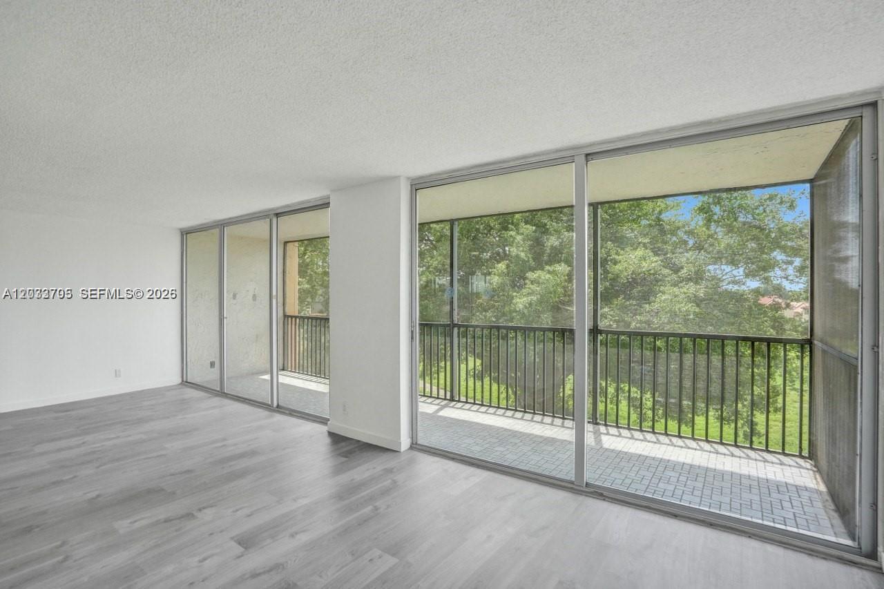 A room with light wood-look flooring features large sliding glass doors opening to a balcony — 3821 Environ Blvd # 403, Lauderhill FL 33319, LAUDERHILL, FL