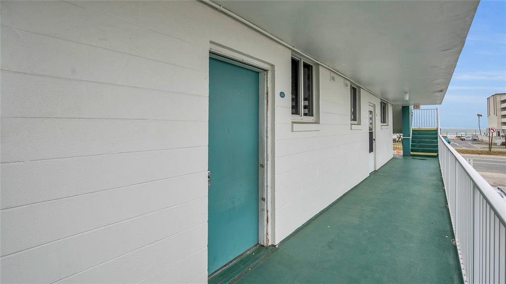 An exterior walkway with a teal door leads to a staircase overlooking the ocean — 2727 N ATLANTIC AVENUE UNIT 2020, DAYTONA BEACH, FL