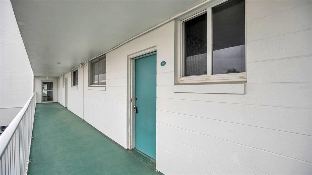 An exterior walkway with a teal door and white concrete block walls leads to unit 202 — 2727 N ATLANTIC AVENUE UNIT 2020, DAYTONA BEACH, FL